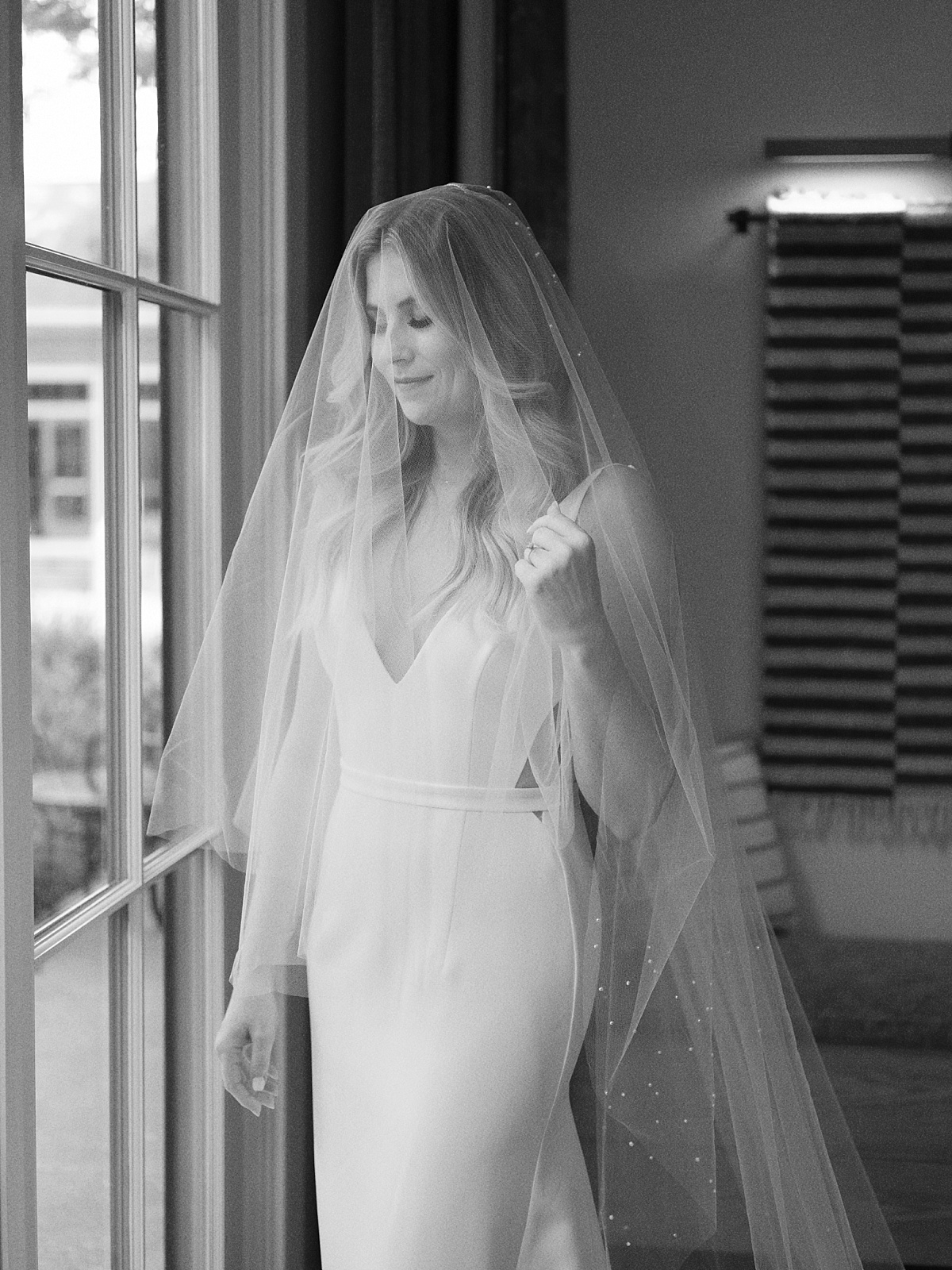 Bride standing in front of a window with her veil over her face.