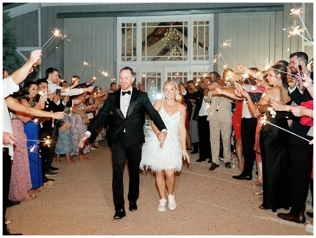Bride and Groom holding hands exiting the barn under a canopy of sparklers their friends are holding. 