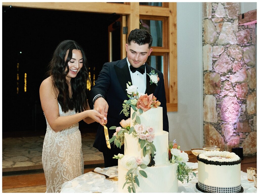 The bride and groom cut their wedding cake together, smiling and laughing in the elegantly adorned reception area.