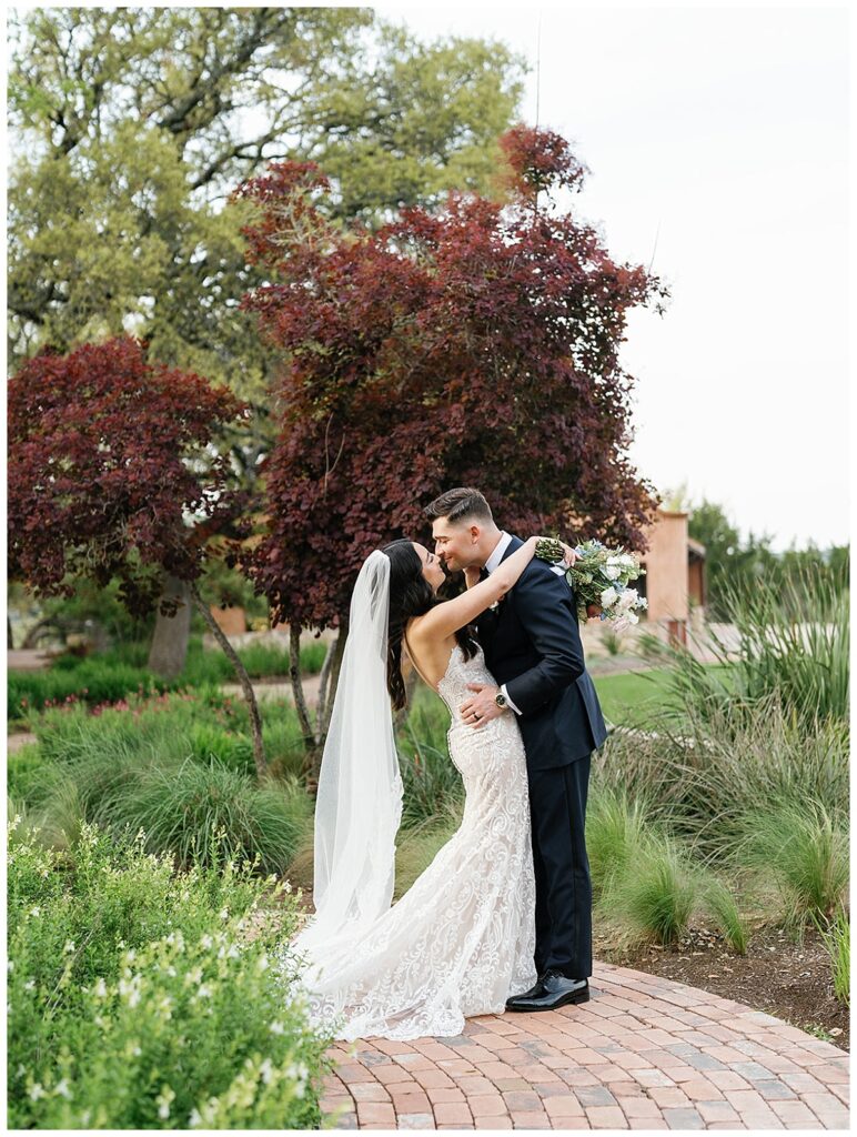 The newlyweds share a kiss in the lush gardens of Camp Lucy, with the charming Ian's Chapel behind them.