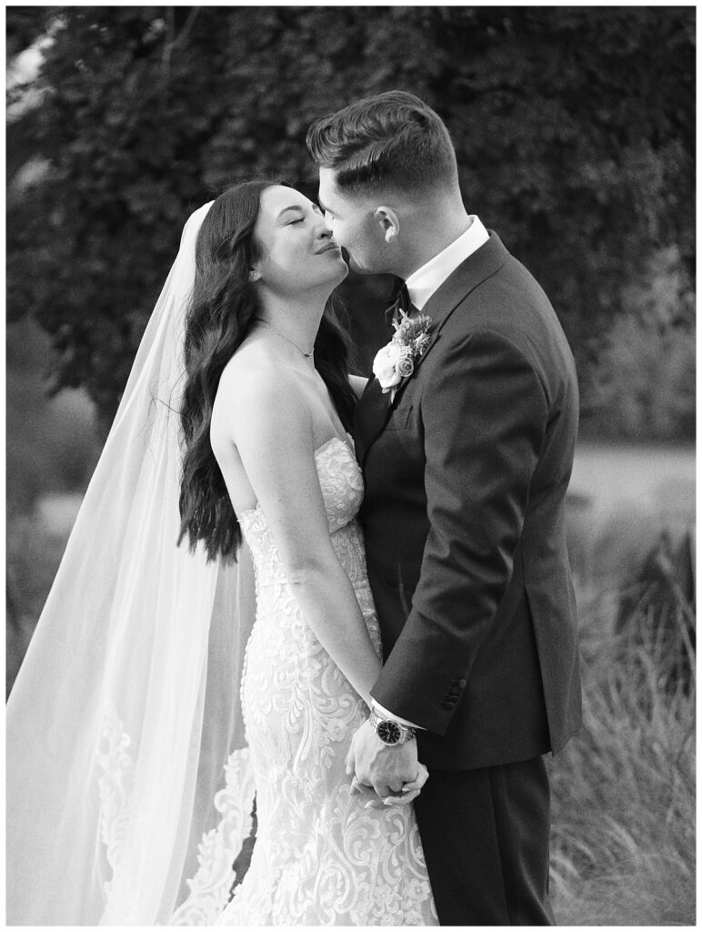 The newlyweds share a kiss in the lush gardens of Camp Lucy, with the charming Ian's Chapel behind them.