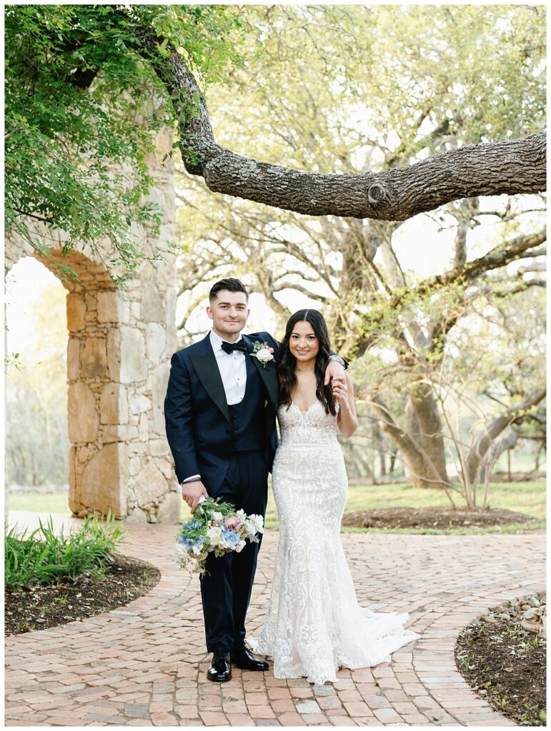 Savana and Casey smile joyfully, standing hand-in-hand on the picturesque grounds of Camp Lucy near Ian's Chapel.